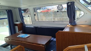Ein Bootsinnenraum mit Holztisch, gepolsterten Sitzgelegenheiten und Fenstern mit Vorhängen.