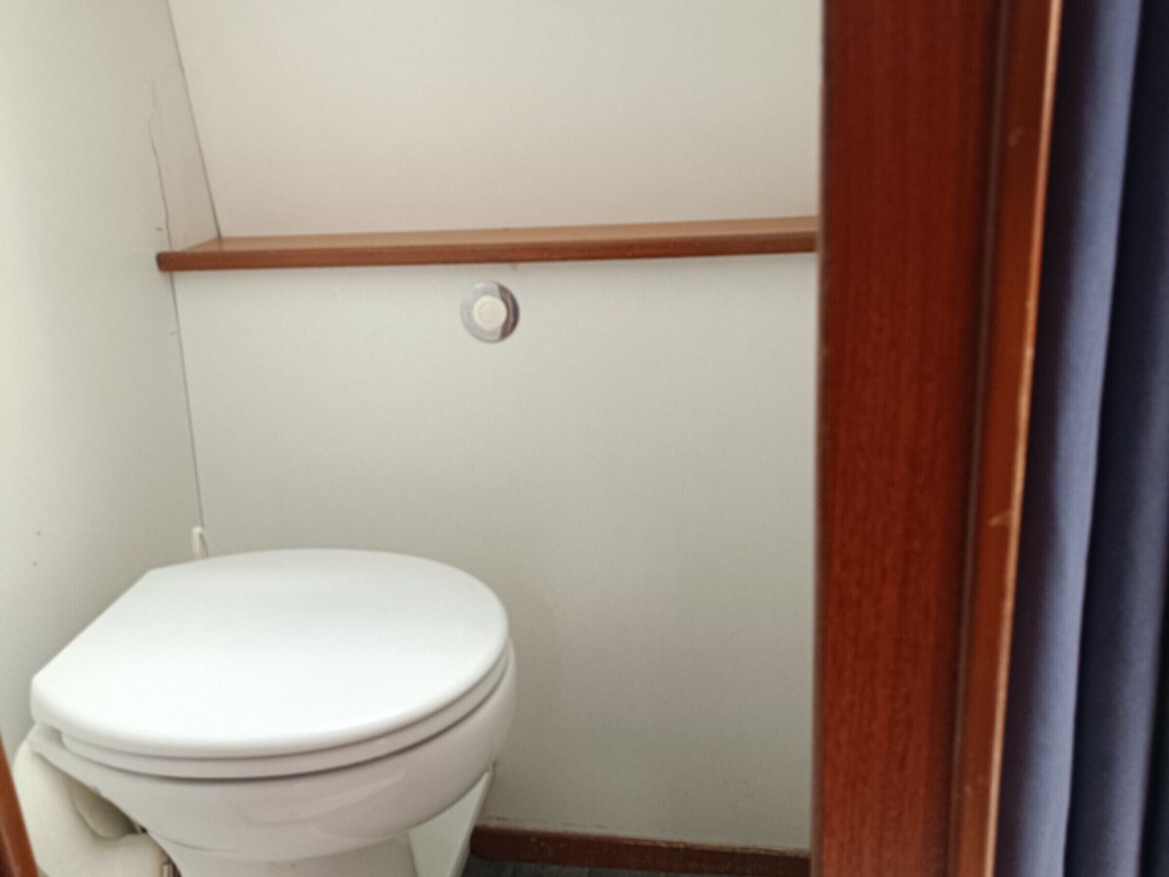 A white toilet with a wooden baseboard, a visible pipe, and a wall-mounted flush handle.