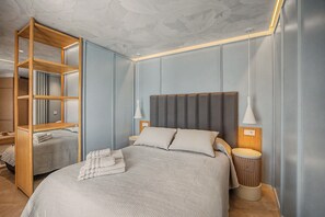 A modern bedroom with a large bed, a wooden shelving unit, and a bedside table with a lamp. - Apartment 'Suite Plaza Conil' with Sea View, Wi-Fi and Air Conditioning (Conil de la Frontera)