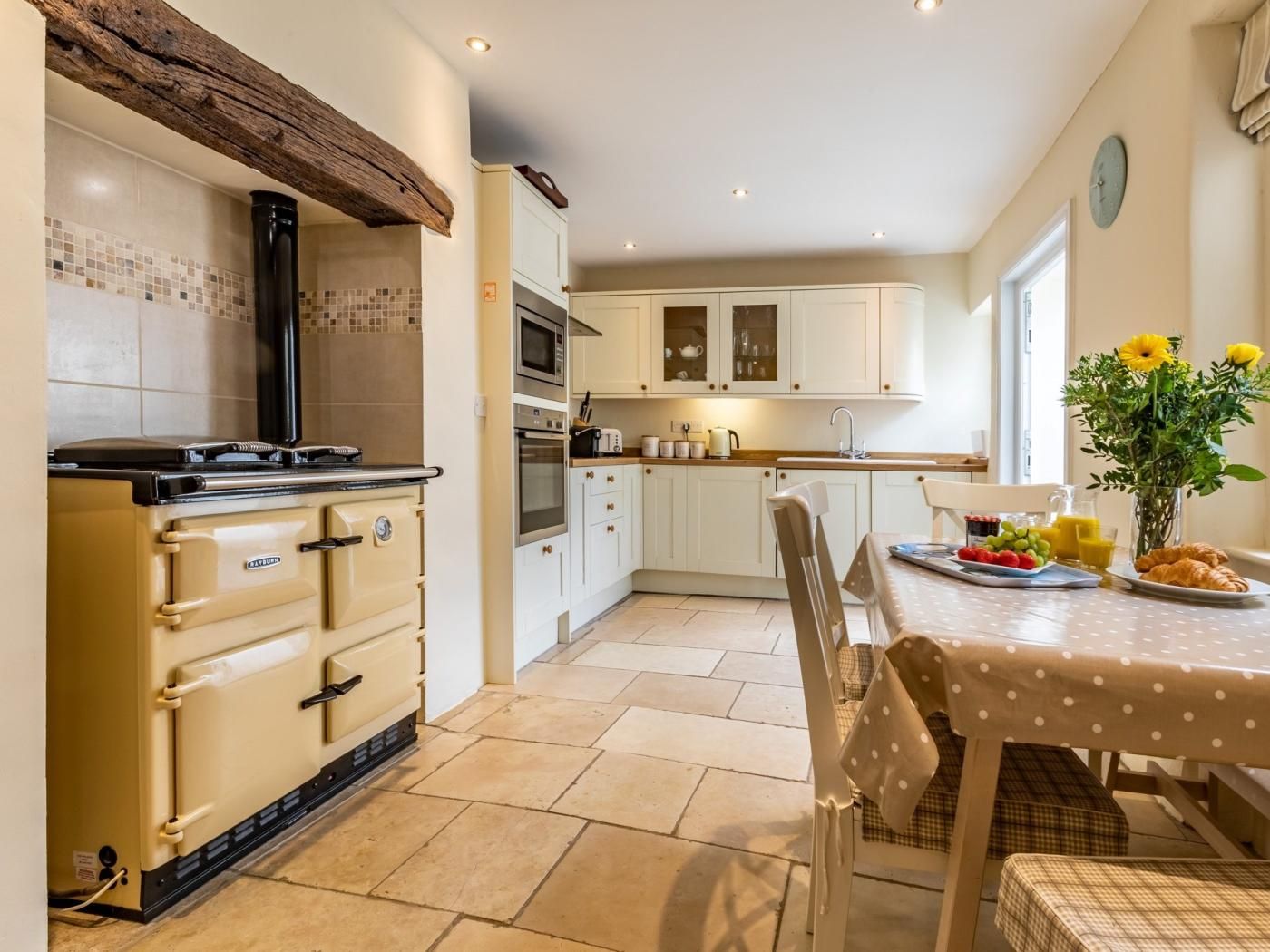 A kitchen with a stove, oven, microwave, and cabinets. There is a dining table with a vase of flowers and a plate of food.