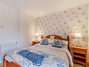 A bedroom with a bed, two bedside tables, a radiator, and a wall with sailboat wallpaper.