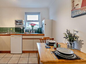 A compact kitchen with a dishwasher, a window with a view, and a dining area with a table set for two. - 1 Bed in Cardigan (oc-moost) (Saint Dogmaels)