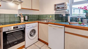 Une cuisine compacte équipée d’un four Bosch, d’un lave-linge et d’un lave-vaisselle, d’une fenêtre avec vue et d’un petit évier.