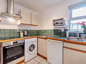 Eine kleine Küche mit Backofen von Bosch, Waschmaschine und Geschirrspüler, einem Fenster mit Blick und einem kleinen Spülbecken.