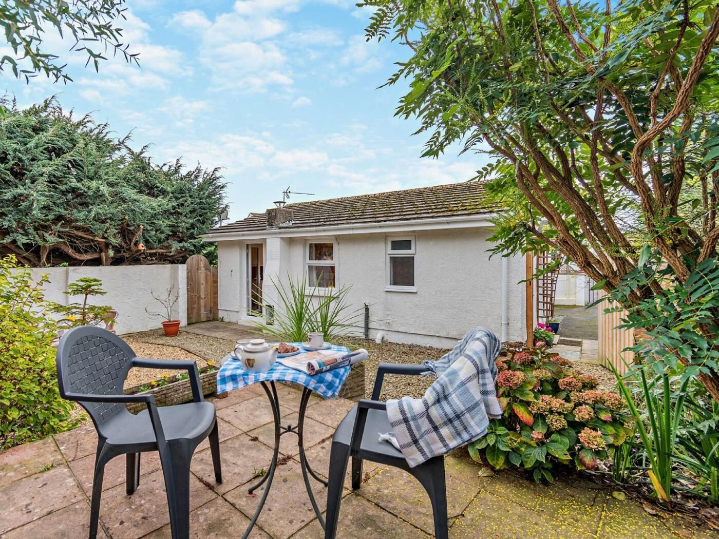 A white house with a tiled roof, a small garden with potted plants, and a table with chairs.