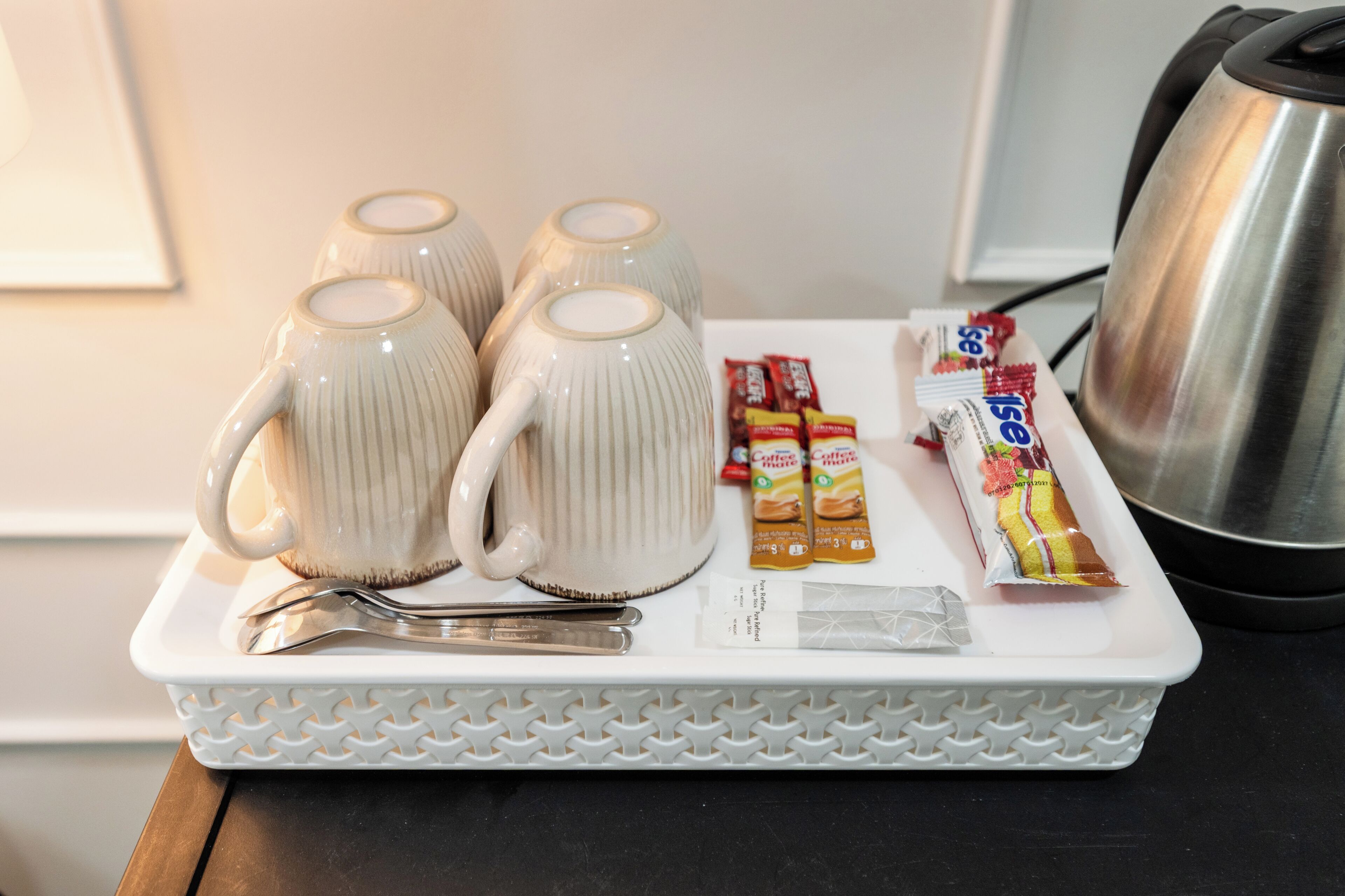 A tray with four ceramic mugs, a spoon, and packets of coffee mate on a white tray.