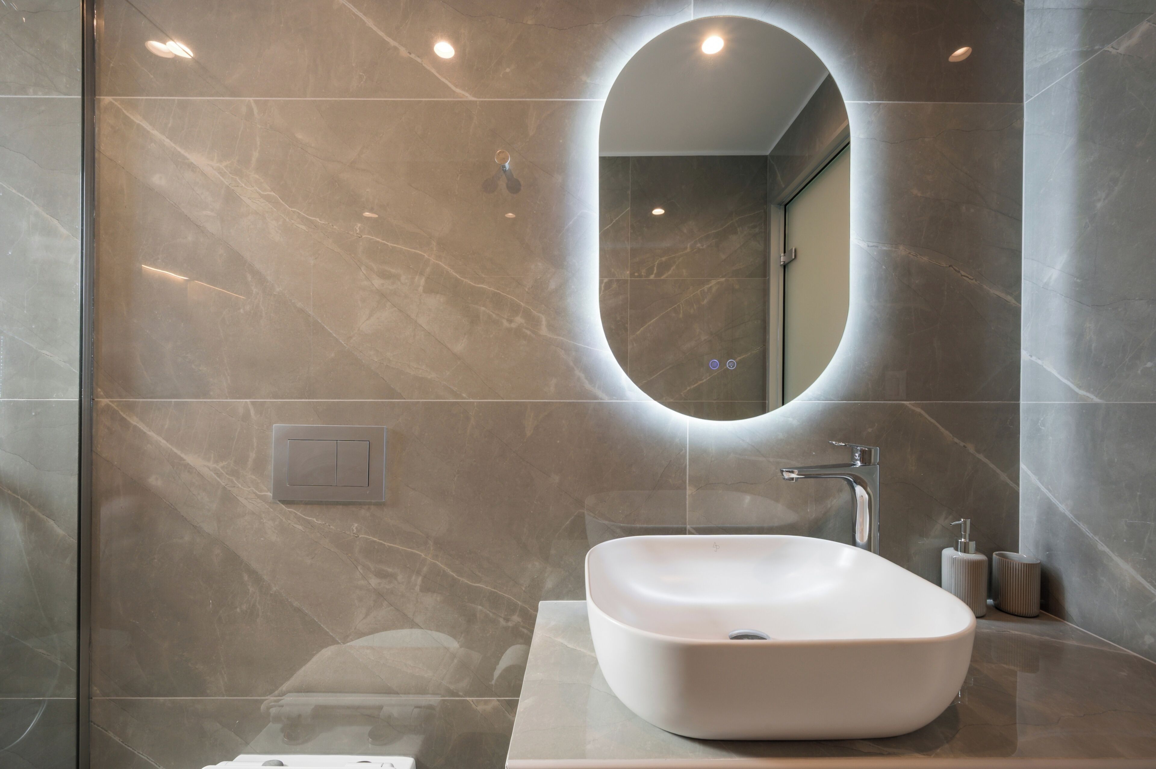 Une salle de bain moderne avec un grand miroir ovale, un lavabo sur colonne et un espace douche.