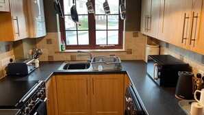 Eine moderne Küche mit Holzschränken, einem Einbauofen, einem Kochfeld, einer Spüle und einem Fenster, an dem Kochutensilien hängen.