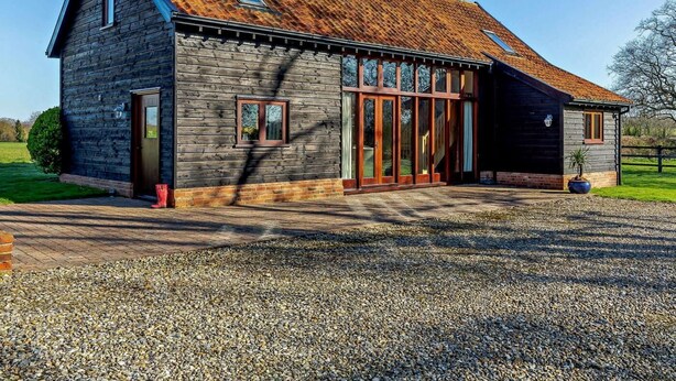 Ein Holzhaus mit geneigtem Dach, großen Fenstern und einer Schotterzufahrt.