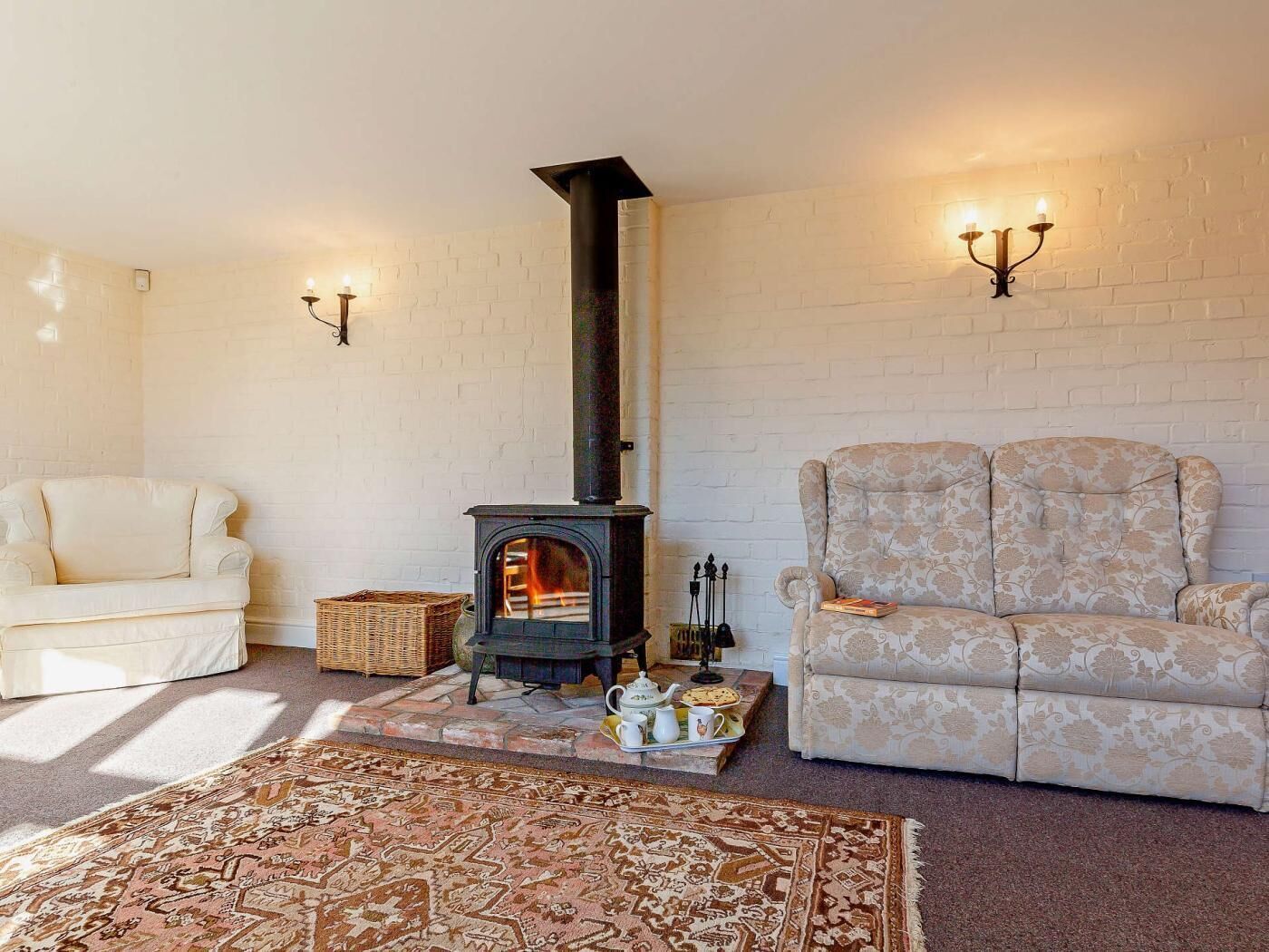 A cozy living room with a fireplace, a white brick wall, a patterned armchair, and a white sofa.
