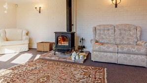 Ein gemütliches Wohnzimmer mit Kamin, einer weißen Ziegelwand, einem gemusterten Sessel und einem weißen Sofa.