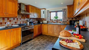 Eine moderne Küche mit Holzschränken, einem Edelstahlherd und einer Frühstückstheke mit Brot und Käse.