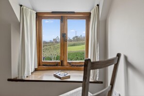 A room with a wooden-framed window, white curtains, a wooden chair, and a small table with glasses and a book. - 2 Bed in Taunton (oc-conco) (Monkton Heathfield)