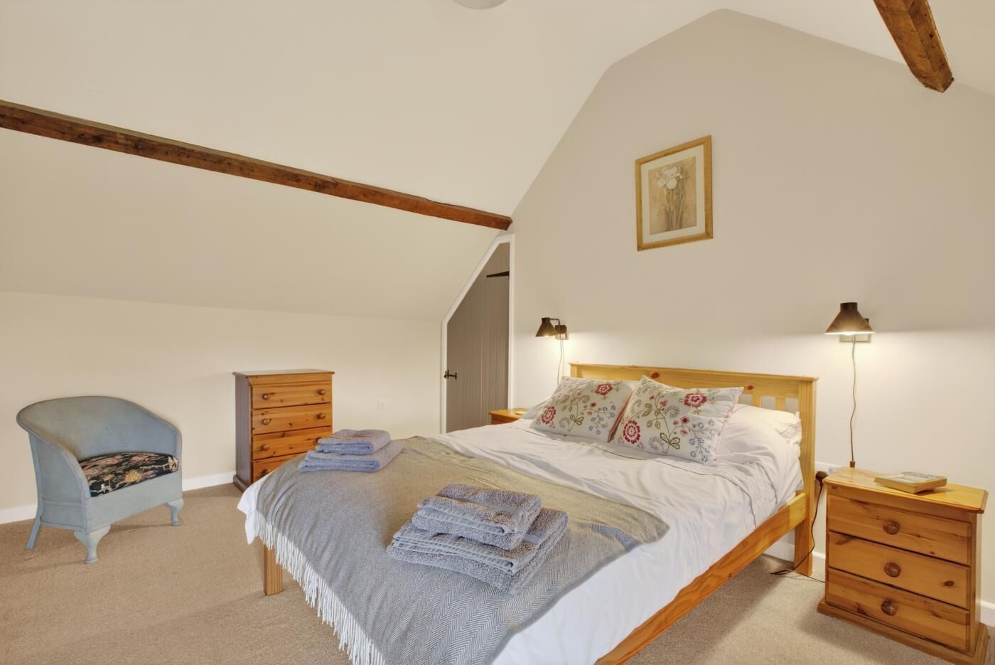 Een slaapkamer met een bed, een stoel, een dressoir en een nachtkastje.