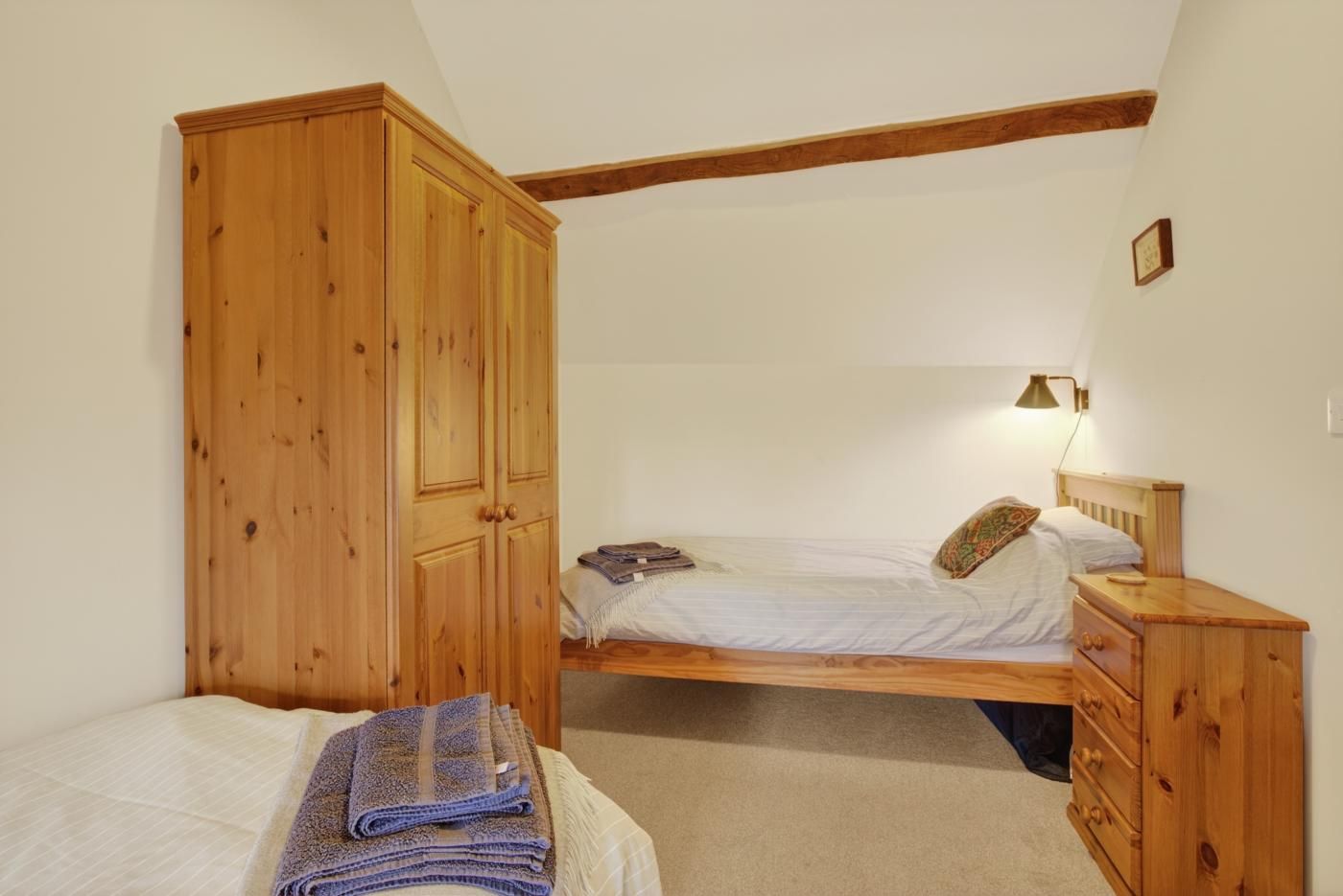 Een slaapkamer met een bed, een houten kledingkast, een nachtkastje en een lamp.