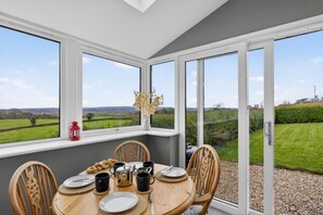 Een eetgedeelte met een tafel voor vier personen, grote ramen en uitzicht op een groen landschap.
