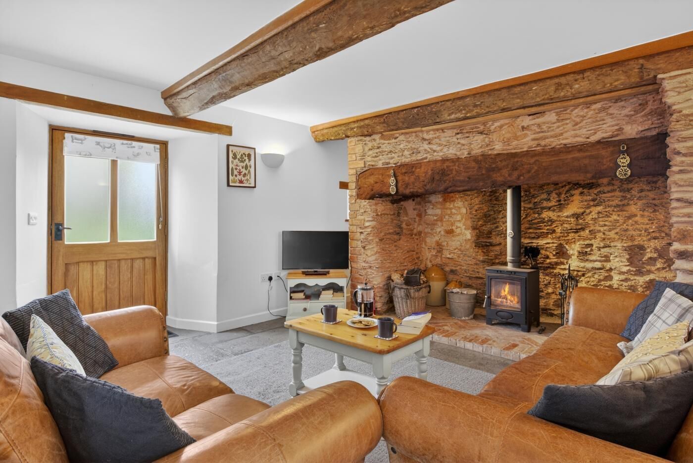 A cozy living room with a stone fireplace, leather sofas, a television, and a coffee table.