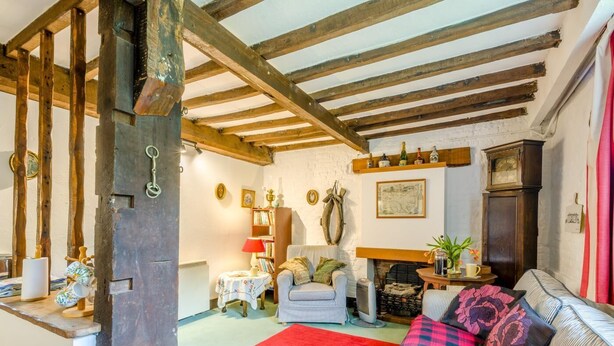 Une pièce rustique avec des poutres apparentes, une cheminée, un canapé, un fauteuil et une bibliothèque.