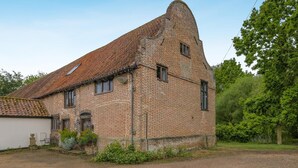 Un bâtiment en briques avec un toit en pente, une petite dépendance attenante et une allée gravillonnée.