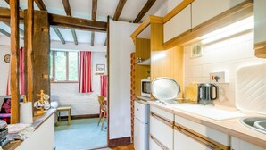 Une cuisine avec des poutres en bois, un coin repas avec une table et des chaises, et une vue sur l’extérieur.