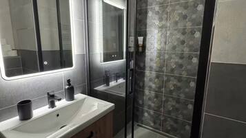 A modern bathroom with a glass-enclosed shower, a large mirror, and a vanity with a sink and cabinets.