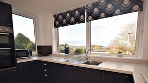 A modern kitchen with dark cabinetry, a built-in oven, a microwave, a sink, and a window with a view of the outdoors. - 2 Bed in Bideford (oc-sandb) (Instow)