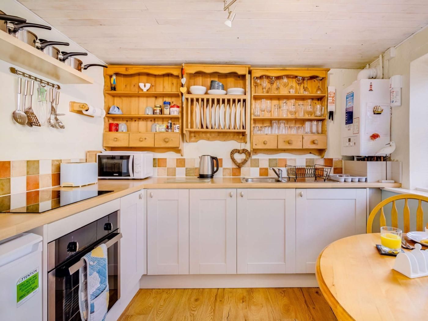 A kitchen with white cabinets, wooden shelves, a microwave, and a sink.
