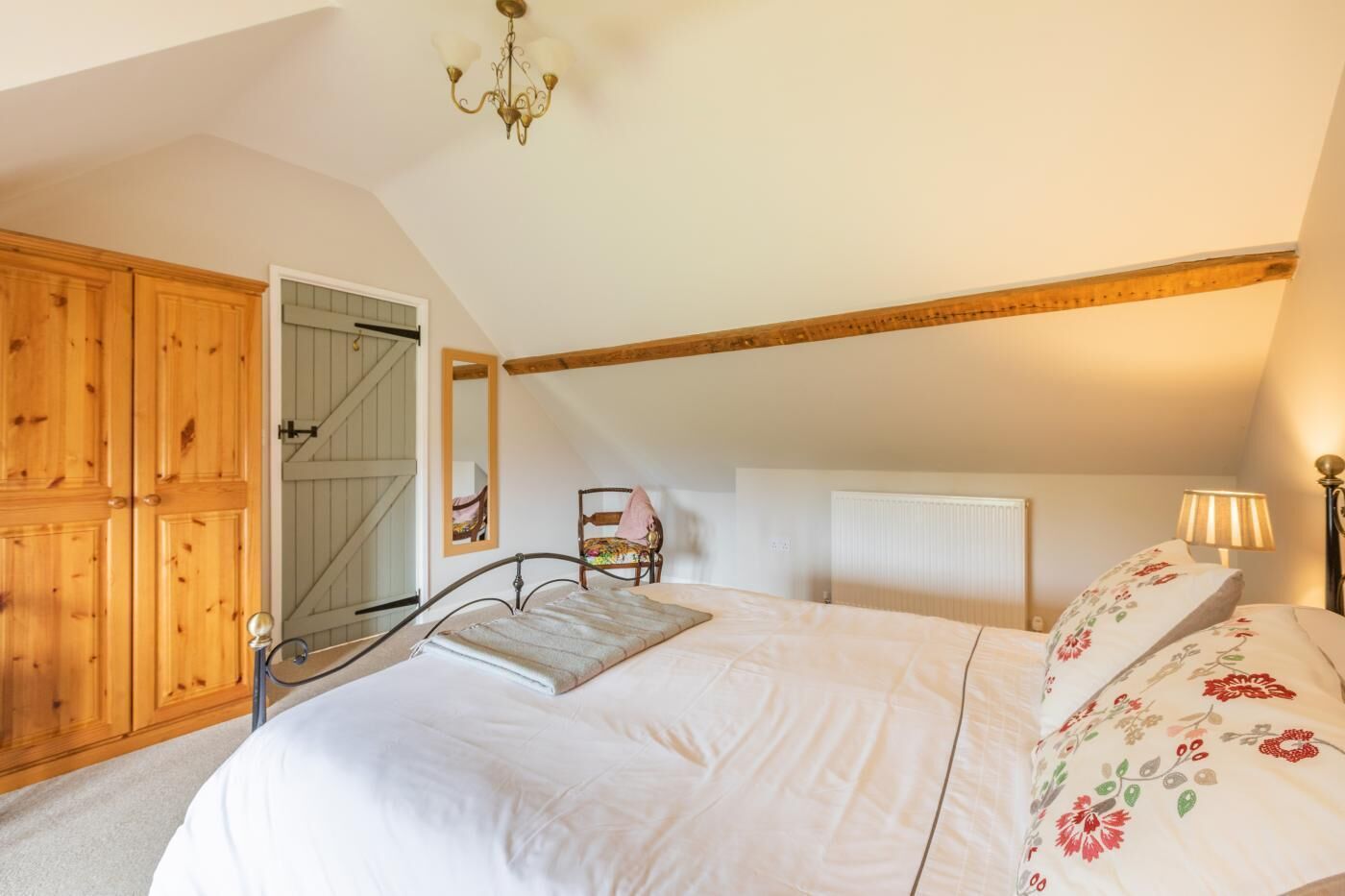 A bedroom with a large bed, wooden wardrobe, and a sloped ceiling.