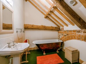 Ein Badezimmer mit einem weißen Waschbecken, einer freistehenden Badewanne, Holzbalken, einer Ziegelwand und einem grünen Boden.