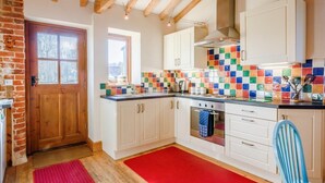 Een keuken met witte kastjes, een betegelde achterwand, een rood tapijt en een houten plafond.