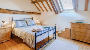 Een slaapkamer met schuine wand, een bed met beddengoed met een patroon, nachtkastjes, een dressingtafel en een raam.
