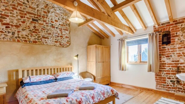 Een slaapkamer met een houten bed, een bakstenen muur, een raam en een houten garderobe.