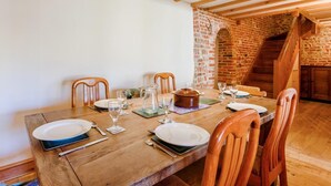 Een eettafel gedekt voor vier personen, met stoelen, een bakstenen muur en een houten trap.