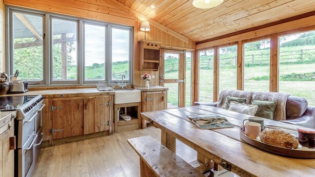 A rustic kitchen with wooden cabinets, a large window, and a dining area with a bench. - 1 Bed in Exeter (oc-lchas) (Cadbury)