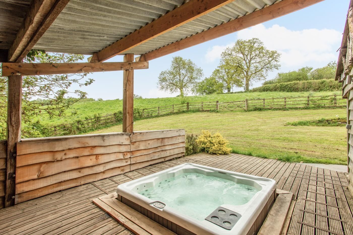 A hot tub on a wooden deck with a view of a grassy field and trees.