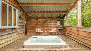 A wooden cabin with a hot tub, two wicker chairs, and a small table. - 1 Bed in Exeter (oc-lchas) (Cadbury)