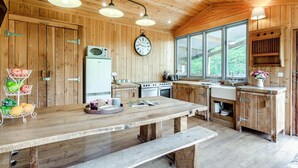 A rustic kitchen with wooden walls, a large window, a clock, and a wooden table with a bench. - 1 Bed in Exeter (oc-lchas) (Cadbury)