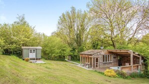 A rustic cabin with a porch, a small shed, and a grassy area with trees. - 1 Bed in Exeter (oc-lchas) (Cadbury)