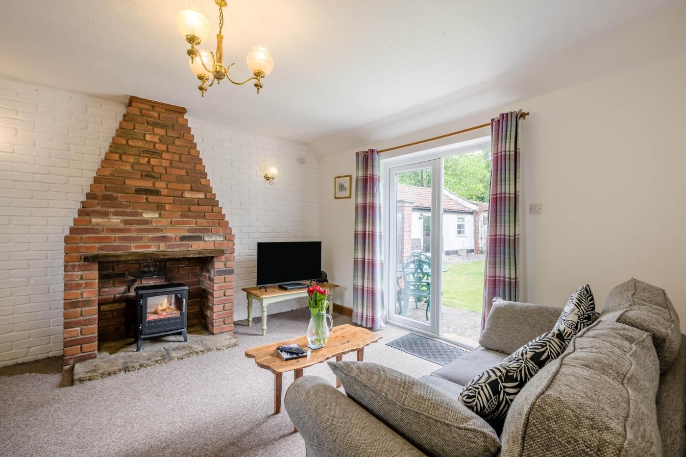 A living room with a brick fireplace, a television, a sofa, and a table with a vase of flowers.