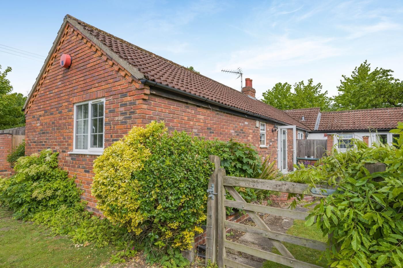 A brick house with a tiled roof, a wooden gate, and a well-maintained garden.