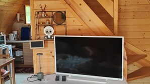 Un intérieur en bois avec un téléviseur posé sur un meuble blanc, une décoration représentant un panda et un coin cuisine.