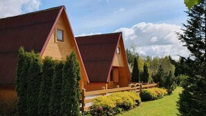 Une cabane en bois avec un toit en pente, entourée d’un jardin bien entretenu et d’une clôture en bois.