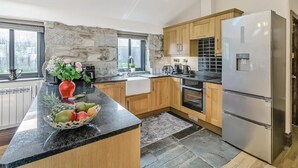 Une cuisine moderne dotée de plans de travail en granit, d’armoires en bois, d’un four encastré et d’un réfrigérateur en acier inoxydable.