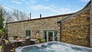 Une maison en pierre dotée d’un jacuzzi, d’un espace salon extérieur et d’une porte donnant sur un patio.