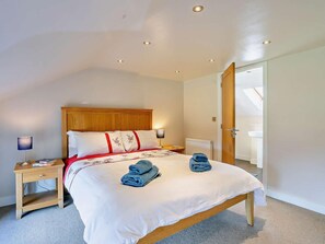 A bedroom with a wooden headboard, a bed with white bedding and red accents, two bedside lamps, a nightstand, and a view of a bathroom through an open door. - 2 Bed in Holmfirth (oc-emley) (New Mill)