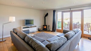 A modern living room with a sofa, TV, fireplace, and a view of the outdoors. - 2 Bed in Holmfirth (oc-emley) (New Mill)