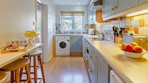 Una cocina compacta con lavadora, una zona de comedor con taburetes y un frutero sobre la encimera.