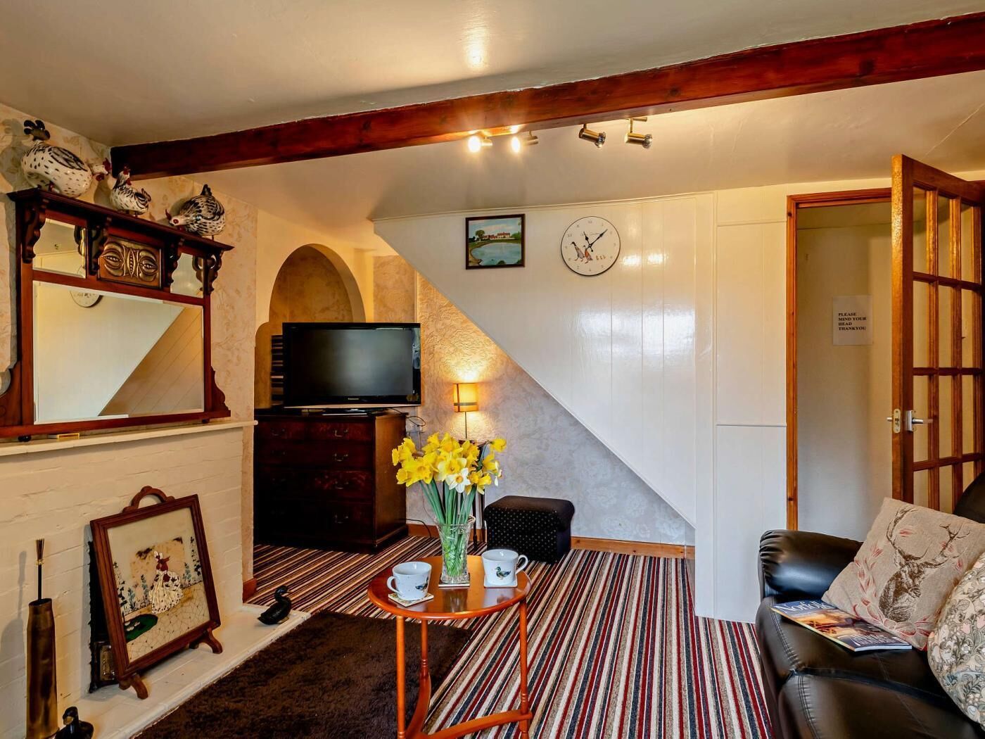 Ein Wohnzimmer mit Fernseher, einer Uhr, einem Kamin, einer Couch und einer Tür mit einem Schild.