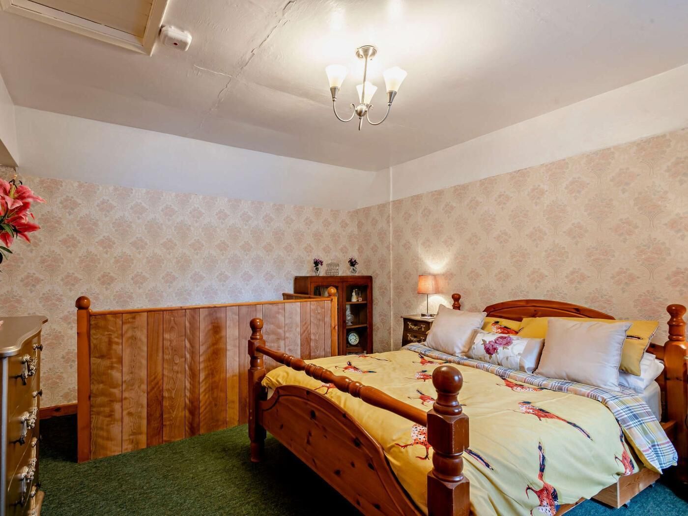 Une chambre à coucher avec un lit en bois, une table de chevet, une lampe et un papier peint à motifs floraux.