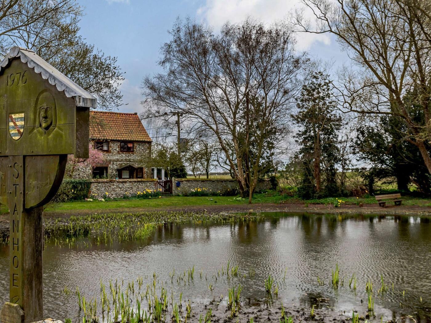 A house with a stone facade, a tiled roof, and a pond in the foreground.